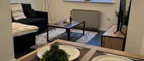 Un comedor con una mesa dispuesta para dos personas, una pequeña planta en maceta y una ventana con persianas.