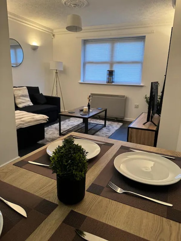 A dining area with a table set for two, a small potted plant, and a window with blinds.