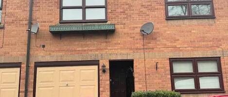 A two-story brick house with a garage, a satellite dish, and a small garden.