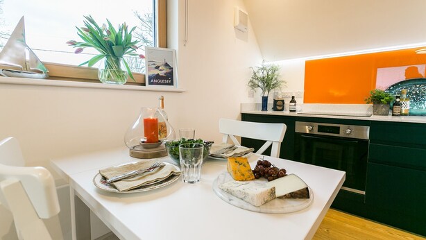 A dining table set with plates, a cheese board, a candle, and a glass of water. - Ty Haul - sleeps 2 guests  in 1 bedroom (Llanfaelog)