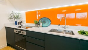 A modern kitchen with a white countertop, black cabinets, and an orange backsplash. - Ty Haul - sleeps 2 guests  in 1 bedroom (Llanfaelog)
