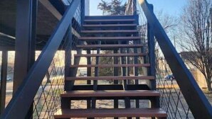 A set of outdoor wooden stairs with metal railings, leading up to a building with a white exterior and a visible window. - Rafton 2 Home (Grafton)