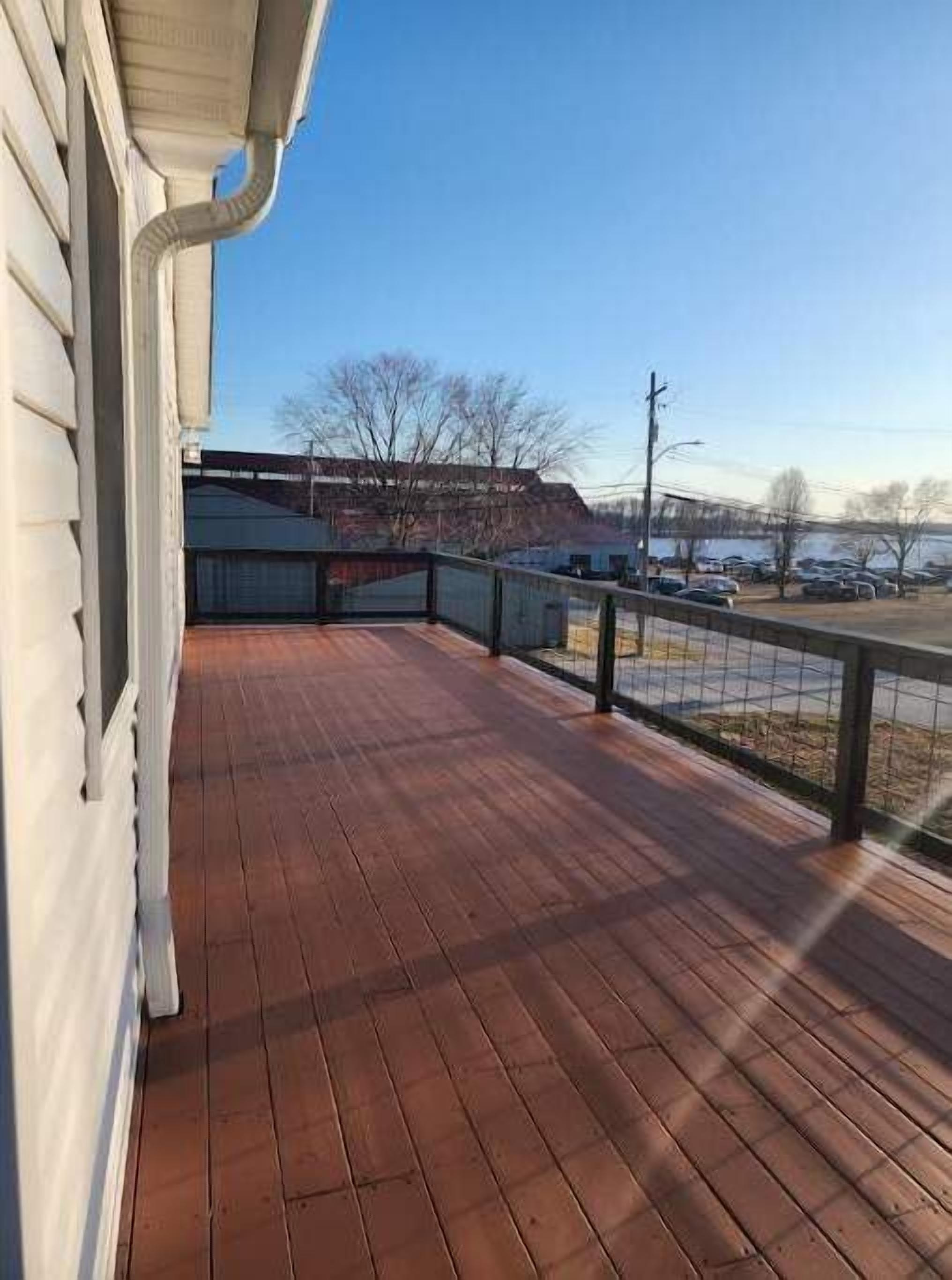 A wooden deck with a railing, a clear sky, and a parking lot in the background.