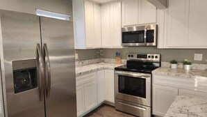 A modern kitchen with stainless steel appliances, white cabinetry, and marble countertops. - Rafton 2 Home (Grafton)