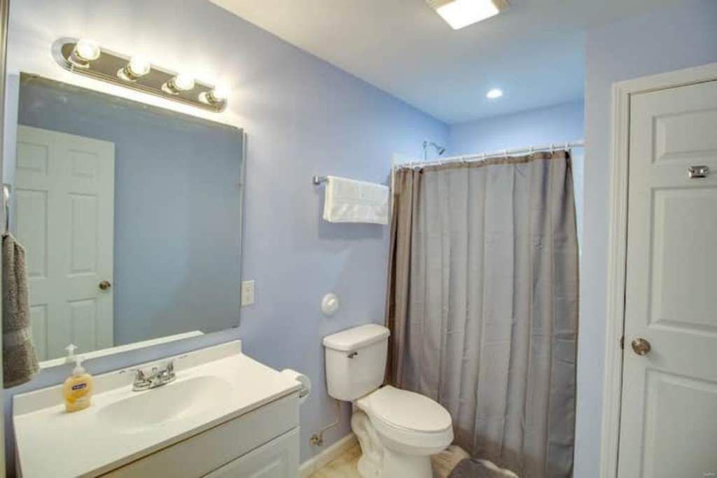 Une salle de bain avec un lavabo blanc, un miroir avec éclairage intégré, des toilettes et un rideau de douche.