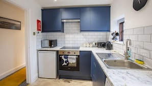 Una cocina compacta con armarios azul oscuro, salpicadero de azulejos blancos y horno empotrado.