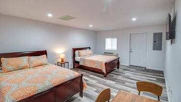 A bedroom with two beds, a wooden table, and a TV mounted on the wall.