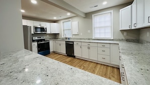 A kitchen with white cabinets, a stainless steel refrigerator, a microwave, a stove, and a dishwasher.