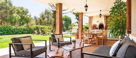 Un patio al aire libre con comedor, asientos y vistas a un jardín y una piscina.