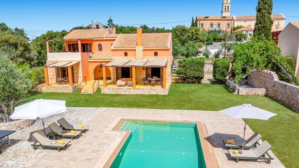 Eine Villa mit Swimmingpool, Sitzgelegenheiten im Freien und Blick auf einen Hügel mit einem Turm.