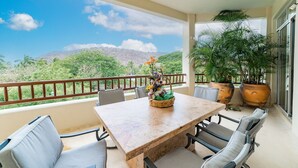 Varanda com mesa e cadeiras, plantas em vasos e vista para uma paisagem montanhosa.