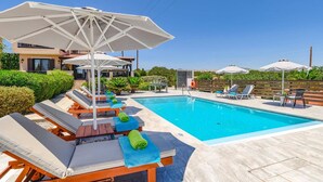 Ein Poolbereich mit Liegestühlen und Sonnenschirmen, ein klares blaues Schwimmbecken und ein Gebäude im Hintergrund.