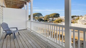 Une terrasse en bois avec une balustrade blanche, une seule chaise Adirondack et une vue sur un quartier résidentiel avec des maisons et des arbres.