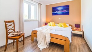 A bedroom with a wooden bed, a chair with a cushion, a painting on the wall, and a window with curtains. - Villa Amalee by Villa Plus (Liznjan)