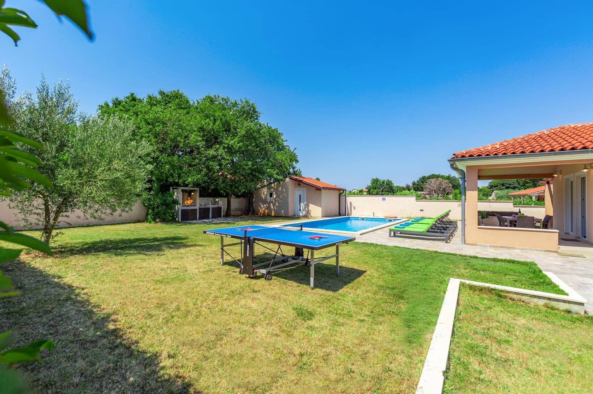 A backyard with a ping pong table, a pool, and a covered seating area.