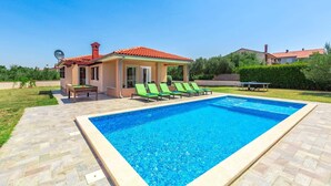 A swimming pool with a tiled deck, a small building with a red roof, and green lounge chairs. - Villa Amalee by Villa Plus (Liznjan)