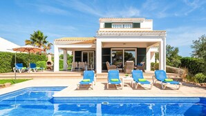 A poolside area with lounge chairs and a building with a tiled roof. - Villa Anchorage by Villa Plus (Puerto Luz)