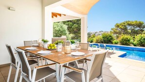 An outdoor dining area with a wooden table and white chairs, overlooking a swimming pool and greenery. - Villa Anchorage by Villa Plus (Puerto Luz)