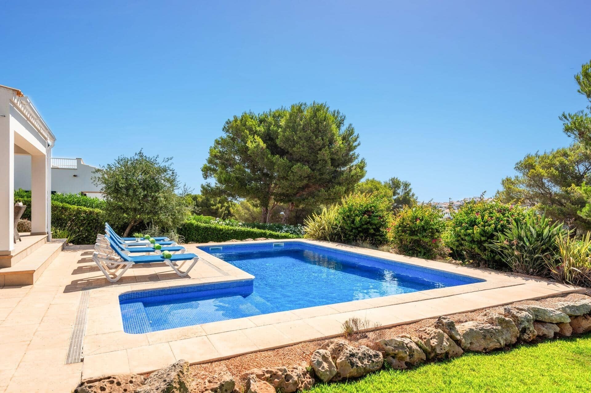 A rectangular swimming pool with a tiled edge, surrounded by a stone border and a grassy area.