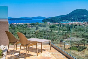 A balcony with two chairs and a table overlooking a coastal town and a bay.