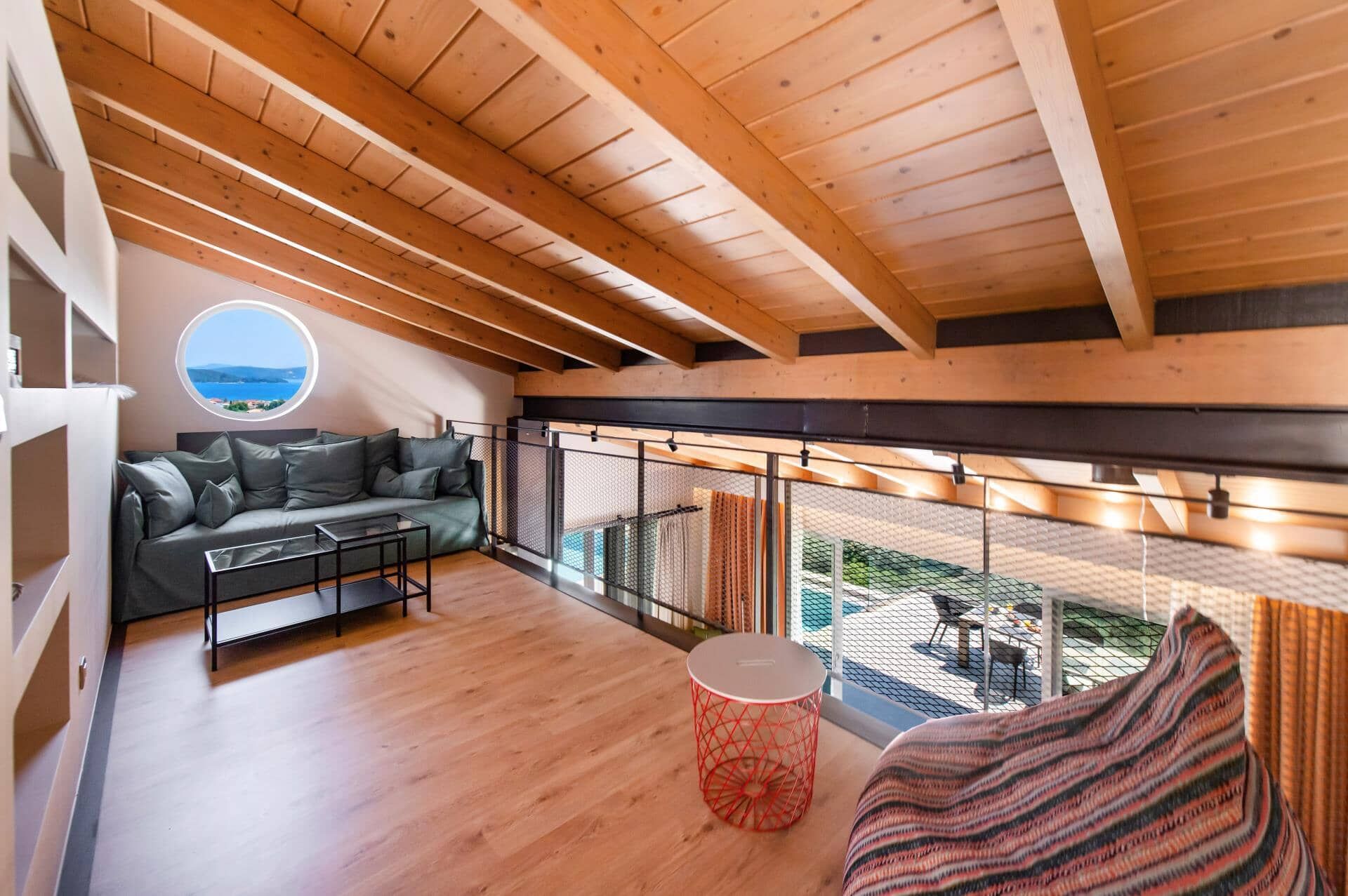 A modern interior with a wooden ceiling, a round window with a view, a sofa, a small table, and a patterned throw.