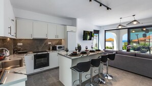 A modern kitchen with a central island, built-in appliances, and a dining area with bar stools. - Villa Annalena by Villa Plus (Malia)