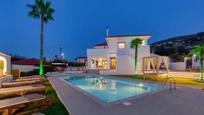 A modern villa with a swimming pool, outdoor seating, and a well-lit patio area. - Villa Annalena by Villa Plus (Malia)