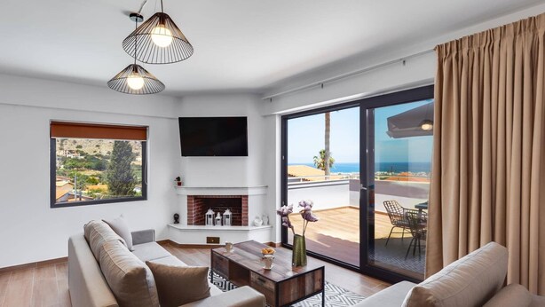 A modern living room with a fireplace, a sofa set, a coffee table, and a view of the sea. - Villa Annalena by Villa Plus (Malia)
