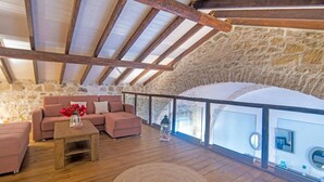 Een gezellig loft slaapkamer met een stenen muur, houten balken, een roze bank en uitzicht naar buiten.
