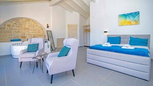 Een moderne slaapkamer met een bed, twee fauteuils, een klein tafeltje, een stenen muur en een badkamer met bad.