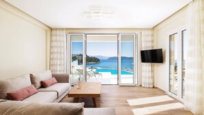 A living room with a sofa, a coffee table, and a TV. It has a large sliding glass door leading to a balcony with a pool and a view of the sea and hills.