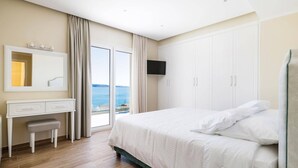 A bedroom with a bed, a desk, a mirror, a TV, and a view of the sea.