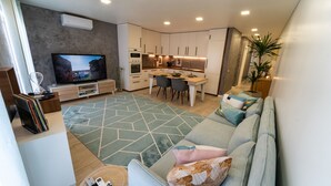 Ein modernes Wohnzimmer mit einer Couch, einem Fernseher und einem Essbereich mit Stühlen und einem Tisch.