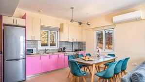 Une cuisine moderne avec des armoires roses, un réfrigérateur en acier inoxydable et un coin repas avec des chaises turquoise et une table en bois.