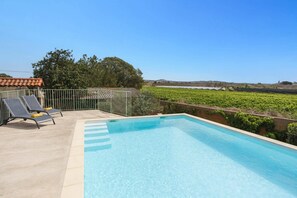 Une piscine avec des chaises longues, une vue sur un vignoble et un ciel dégagé.