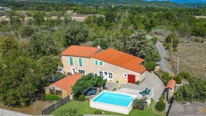 Una casa de dos pisos con piscina, rodeada de vegetación y colinas.