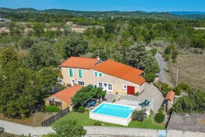 A two-story house with a swimming pool, surrounded by greenery and hills.