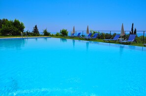 Relax by the serene pool surrounded by lush greenery and lounge chairs with umbrellas.