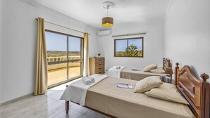 Une chambre avec deux lits, une grande fenêtre donnant sur un beau paysage, un luminaire au plafond et une tête de lit en bois.
