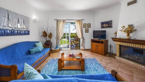 Ein Wohnzimmer mit blauem Sofa, Couchtisch aus Holz, Fernseher und Kamin.