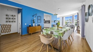 A modern kitchen with white cabinets, a blue accent wall, and a dining area with a green tablecloth. - Villa Casa Duarte by Villa Plus (Olhos de Água)