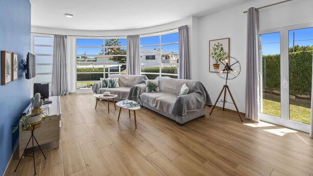 A spacious living room with a large window, a sofa, a coffee table, and a floor lamp. - Villa Casa Duarte by Villa Plus (Olhos de Água)