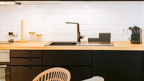 A modern kitchen with dark cabinets, a white tiled backsplash, a black faucet, and a wooden chair. - FLH Caparica By the Sea with Balcony (Almada)