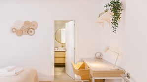 A minimalist bedroom with a wooden desk, a chair, a bed, and a bathroom visible through an open door. - FLH Caparica By the Sea with Balcony (Almada)