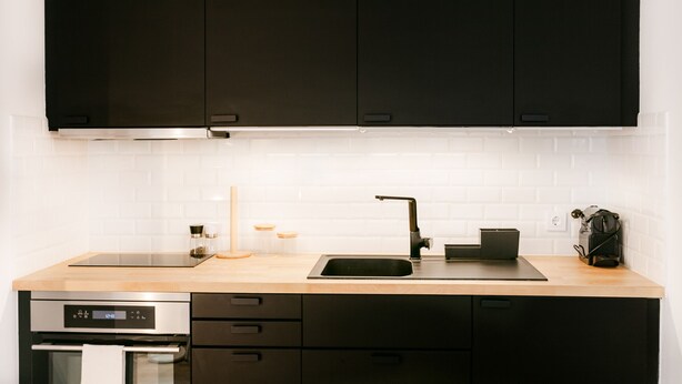 A modern kitchen with black cabinets, a stainless steel sink, and a built-in oven. - FLH Caparica By the Sea with Balcony (Almada)