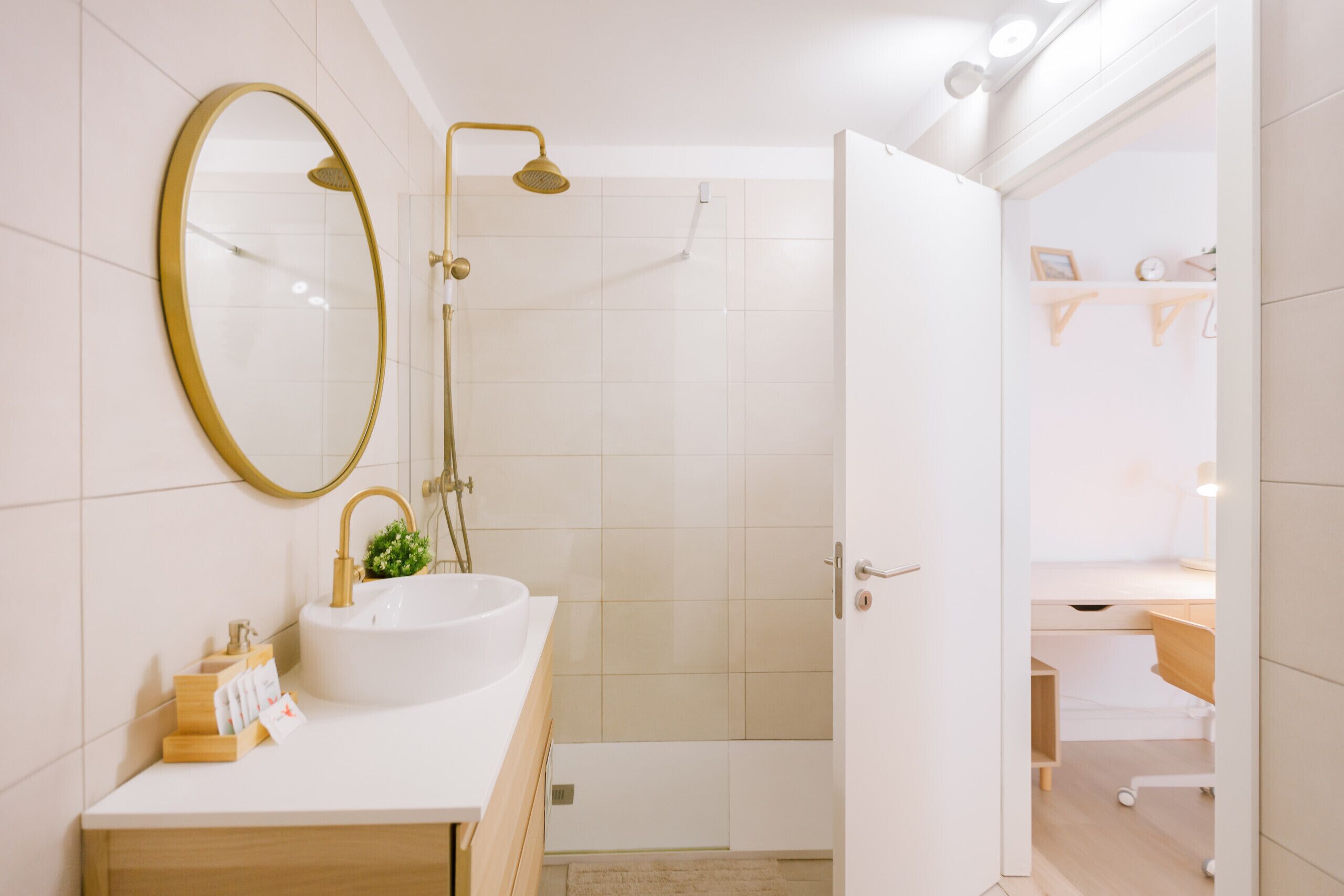 A bathroom with a white sink, gold fixtures, a large mirror, and a shower area.