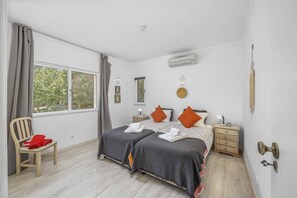 A bedroom with two beds, a chair, a nightstand, a lamp, and a window with curtains. - Villa Casa Pimenteira by Villa Plus (Lagoa)