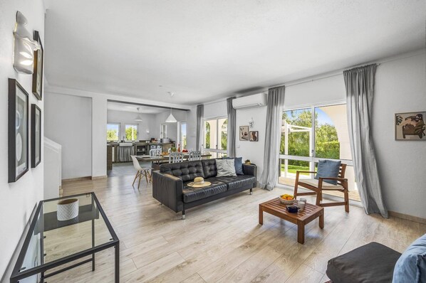 A spacious living room with a black leather sofa, a wooden coffee table, and a dining area with a white table and chairs.