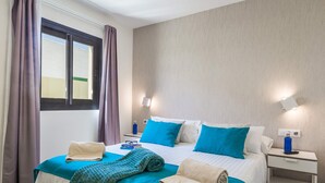 A hotel room with a bed, two bedside tables, a window with curtains, and a wall-mounted light fixture. - Villa Del Mar by Villa Plus (Caleta de Fustes)