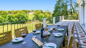Un espace de restauration en plein air avec une table dressée pour deux personnes, comprenant des verres à vin, des assiettes et une baguette.
